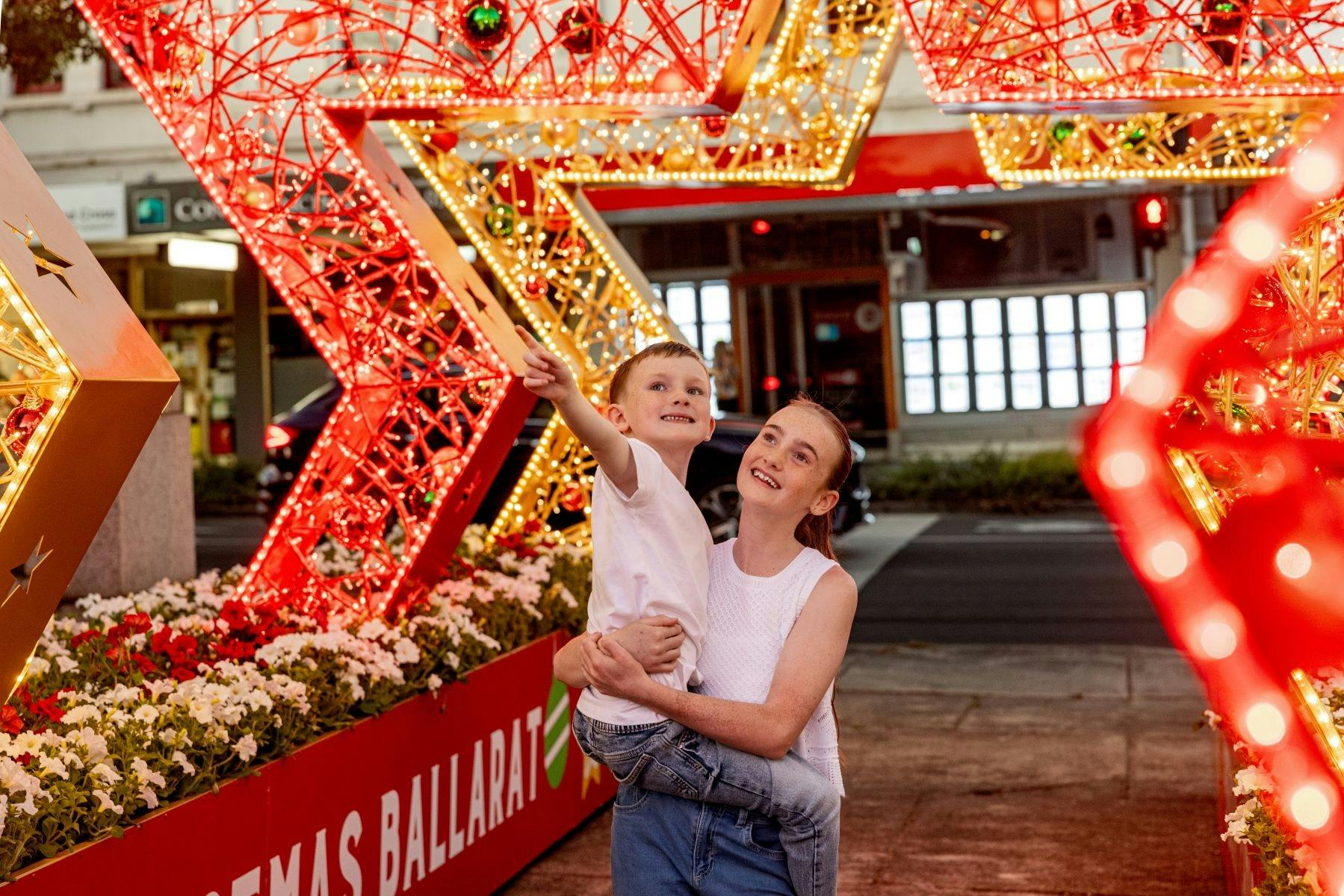 A girl holds a young boy who is pointing to the star archway they are standing under