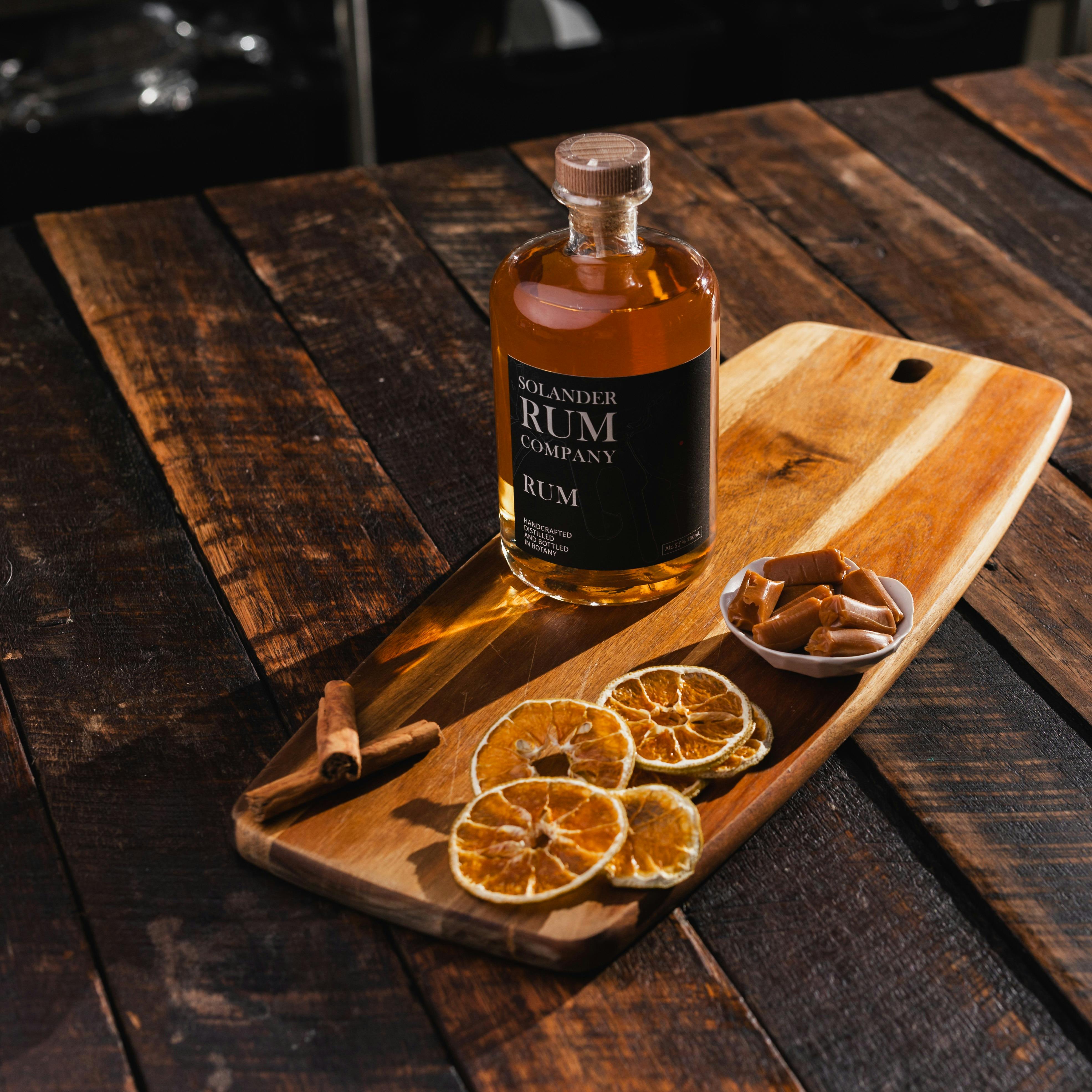 A bottle of rum on a wooden board with orange wheels  and cinnamon sticks