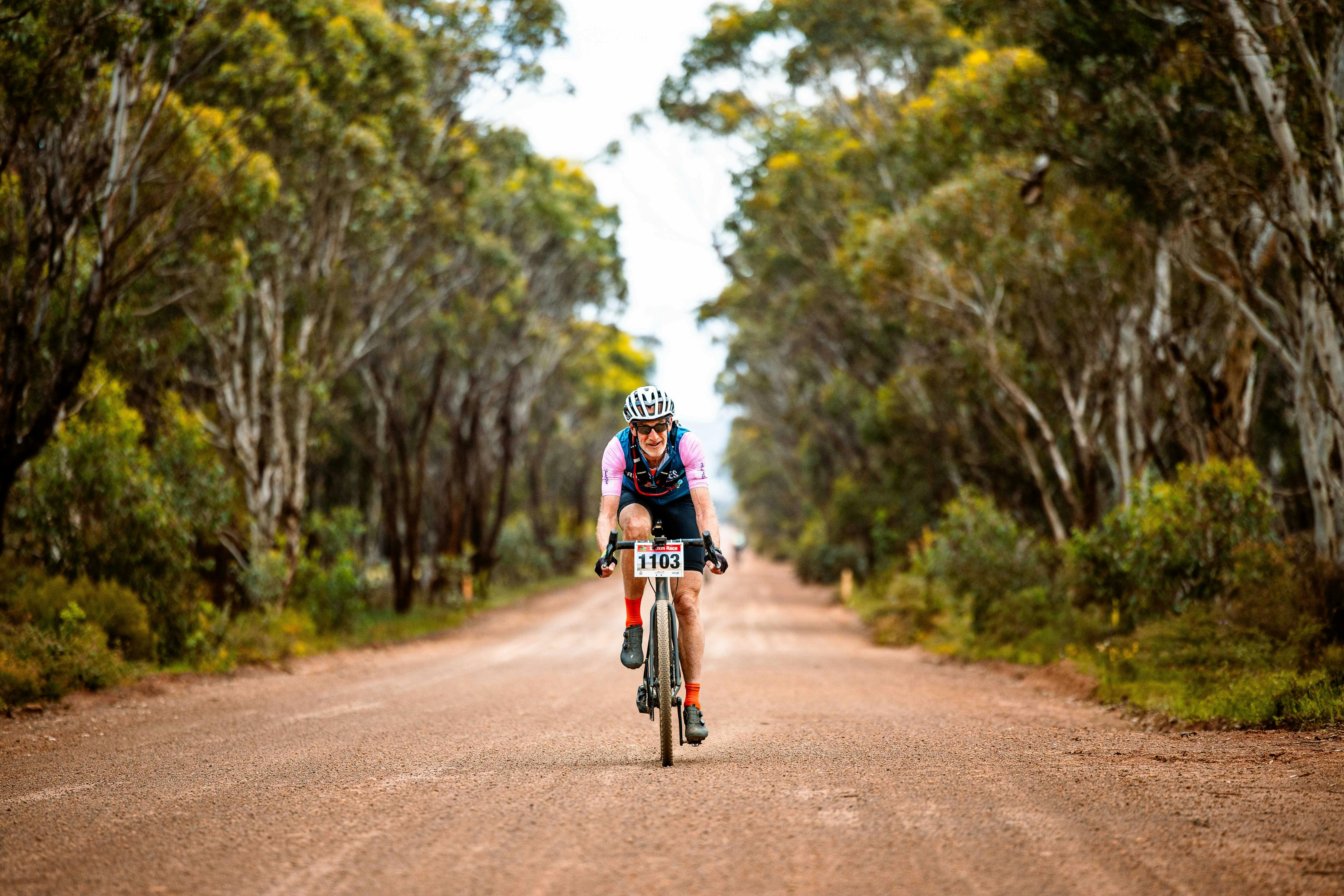 Gravel cyclist on tree/bush lined gravel road