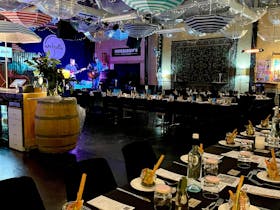 Long tables set up in a live music venue with umbrellas hanging from the  roof