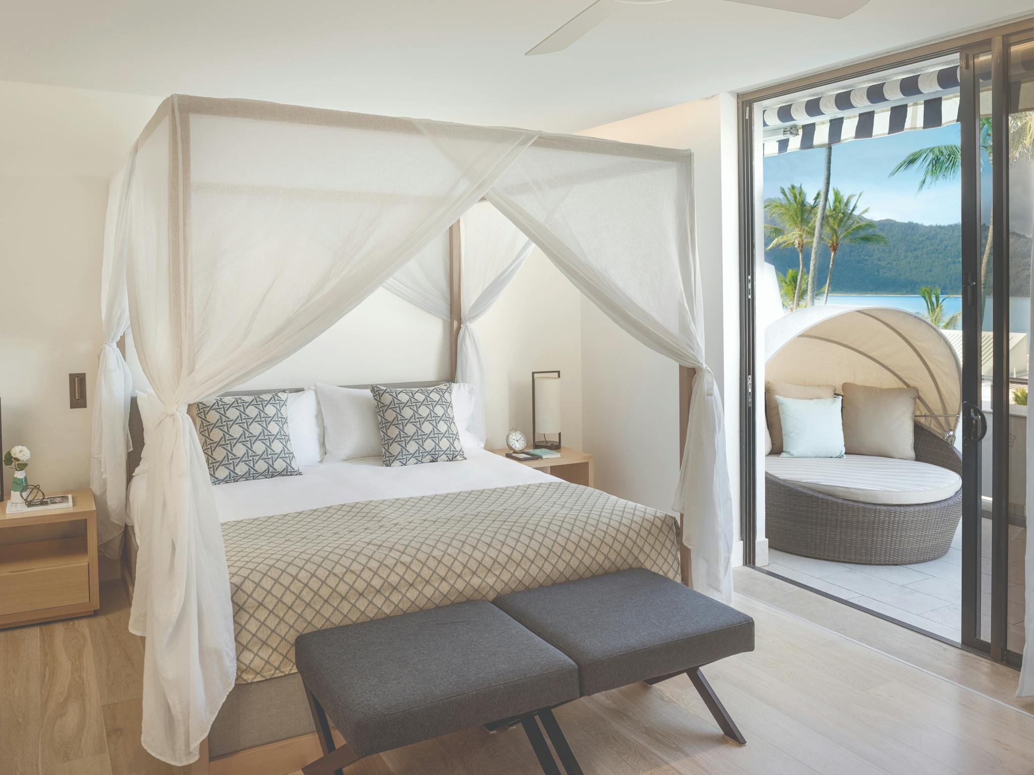 Bedroom with a canopy bed, elegant linens, nightstands, and a balcony featuring ocean views Bedroom with a canopy bed, elegant linens, nightstands, and a balcony featuring ocean views