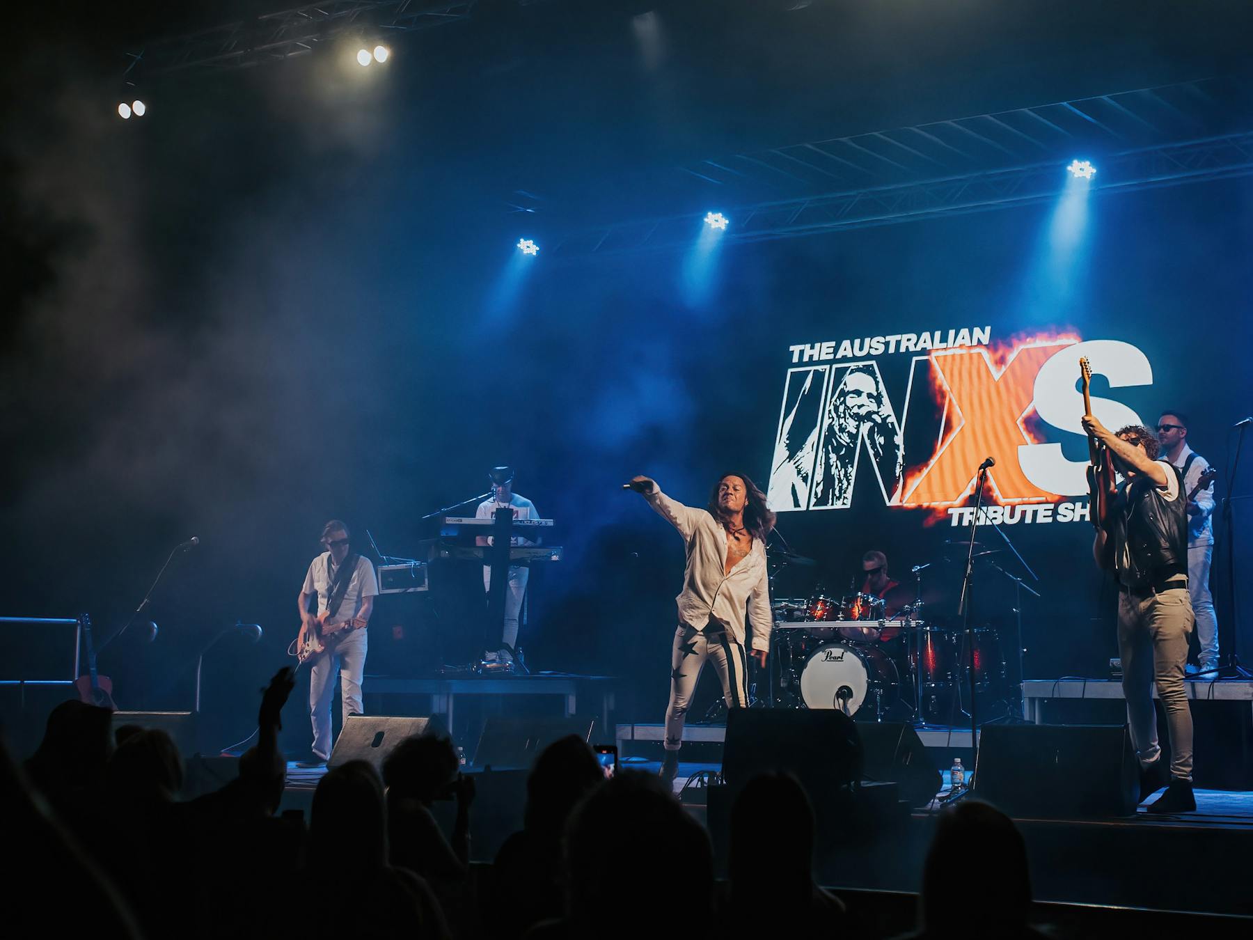 Four band members including Dellacoma Rio on stage, playing guitars, piano and drums
