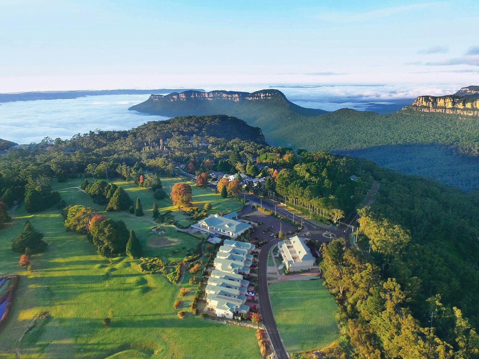 Aerial view of a mountain retreat surrounded by bushland, gardens and open lawns.