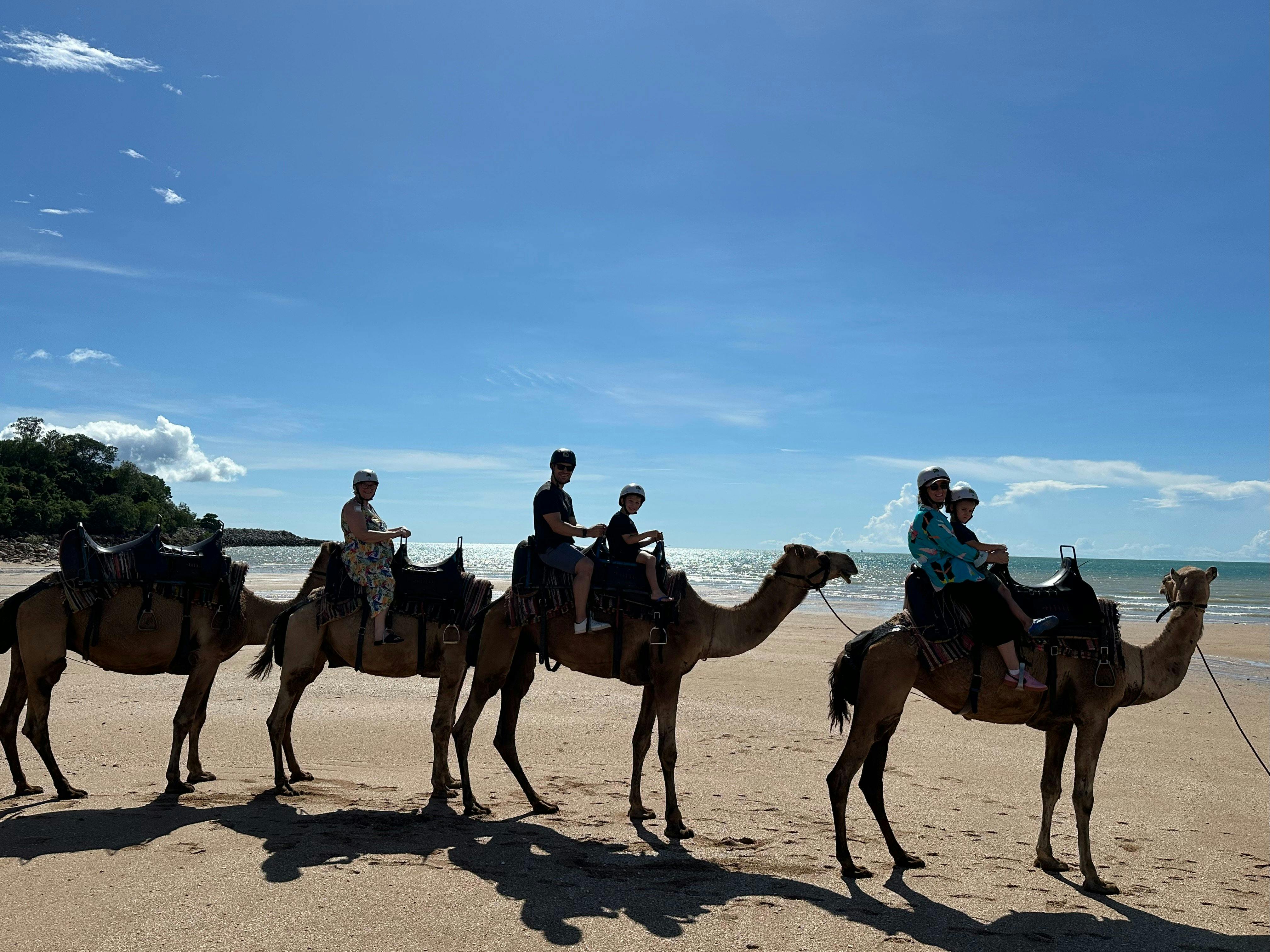 Riders on camels enjoy a sunny beach ride with ocean views and blue skies in the heart of Darwin
