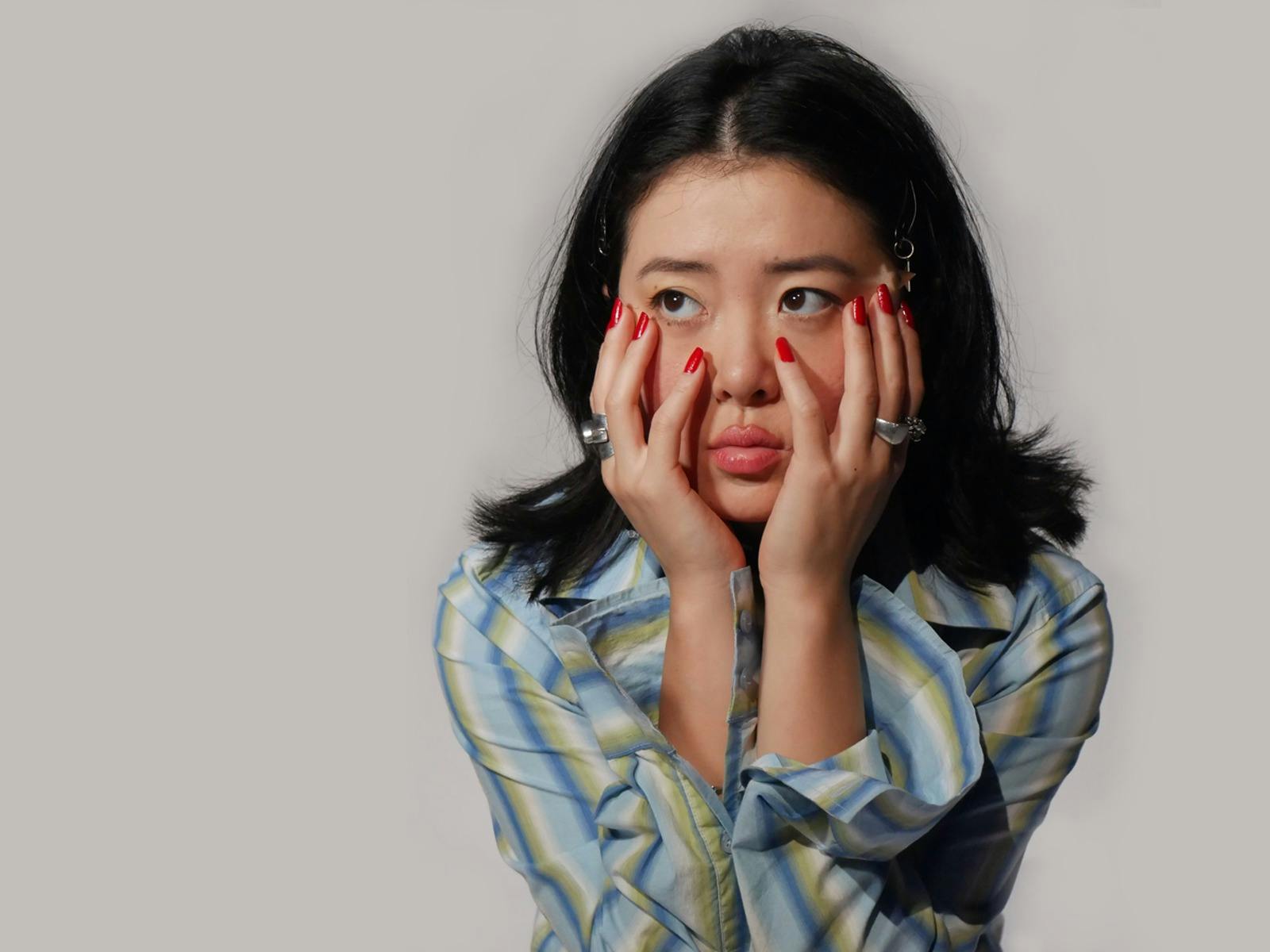 a young fashionable woman clutches her face looking bored and unsure