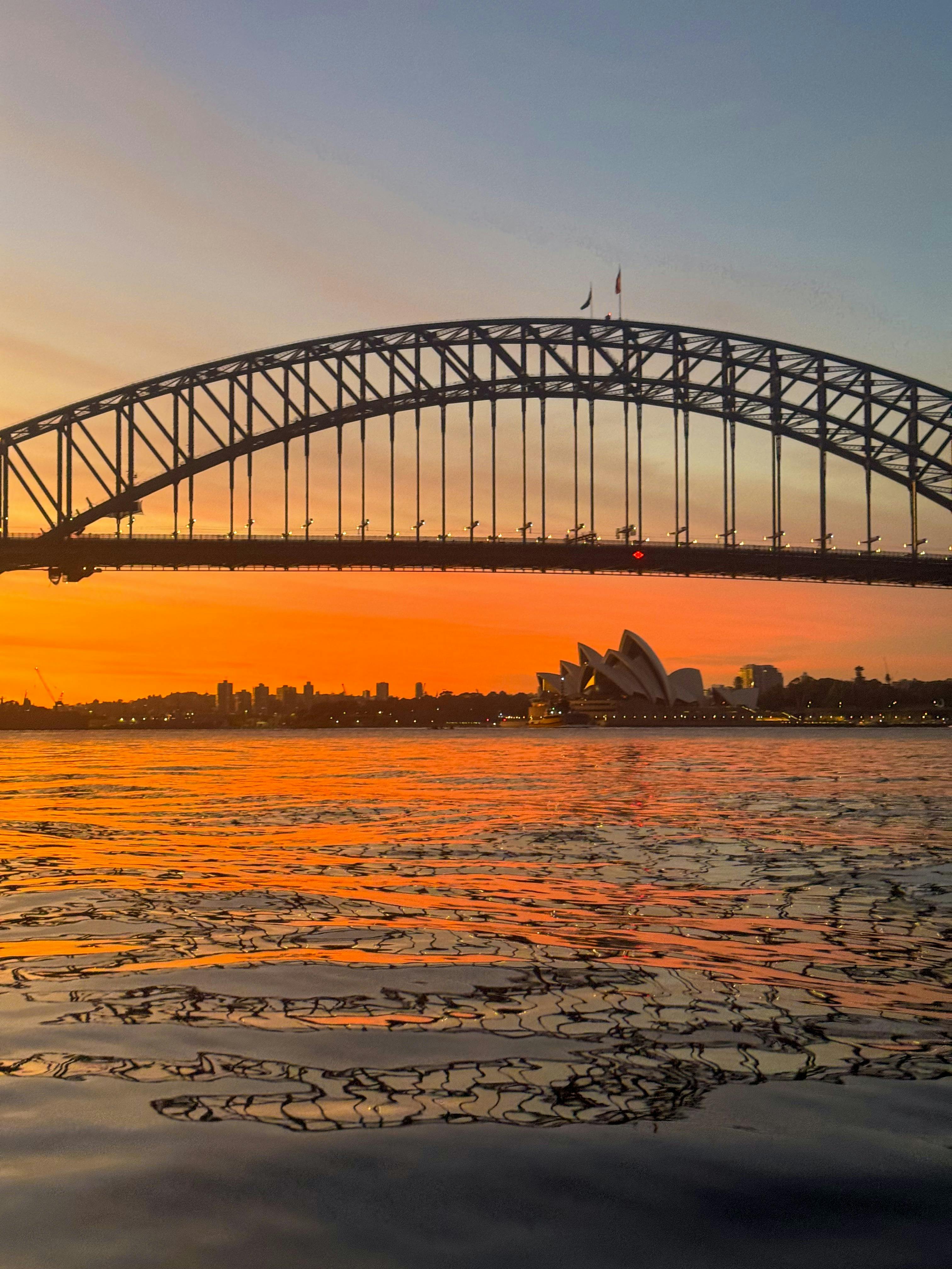 Orangefarbener Sonnenaufgang über dem Hafen von Sydney mit der Silhouette des Opernhauses und der Sydney Harbour Bridge
