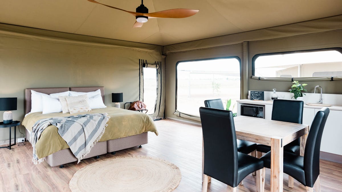 Inside spacious glamping tent with large bed, ceiling fan and dining table