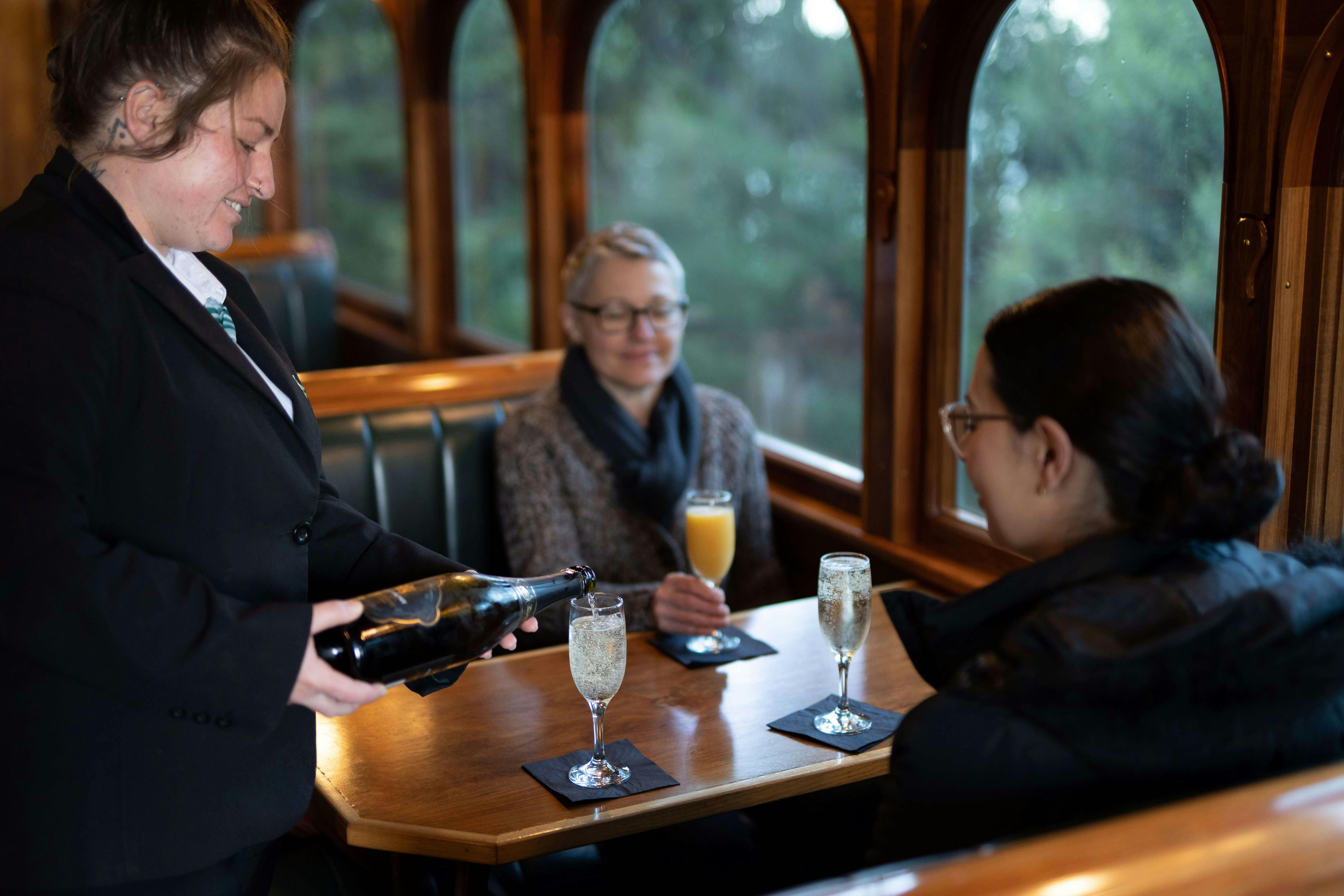 Staff member pours sparkling wine for passengers onboard the wilderness carriage