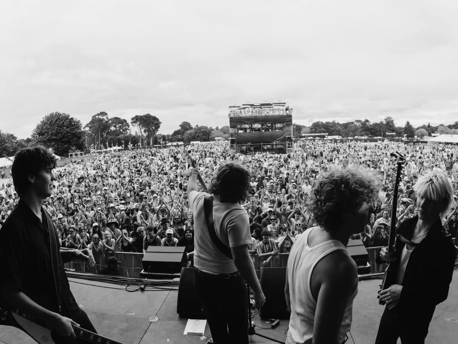 Live shot of The Rions on stage at a festival with a huge crowd. Photo is black and white.