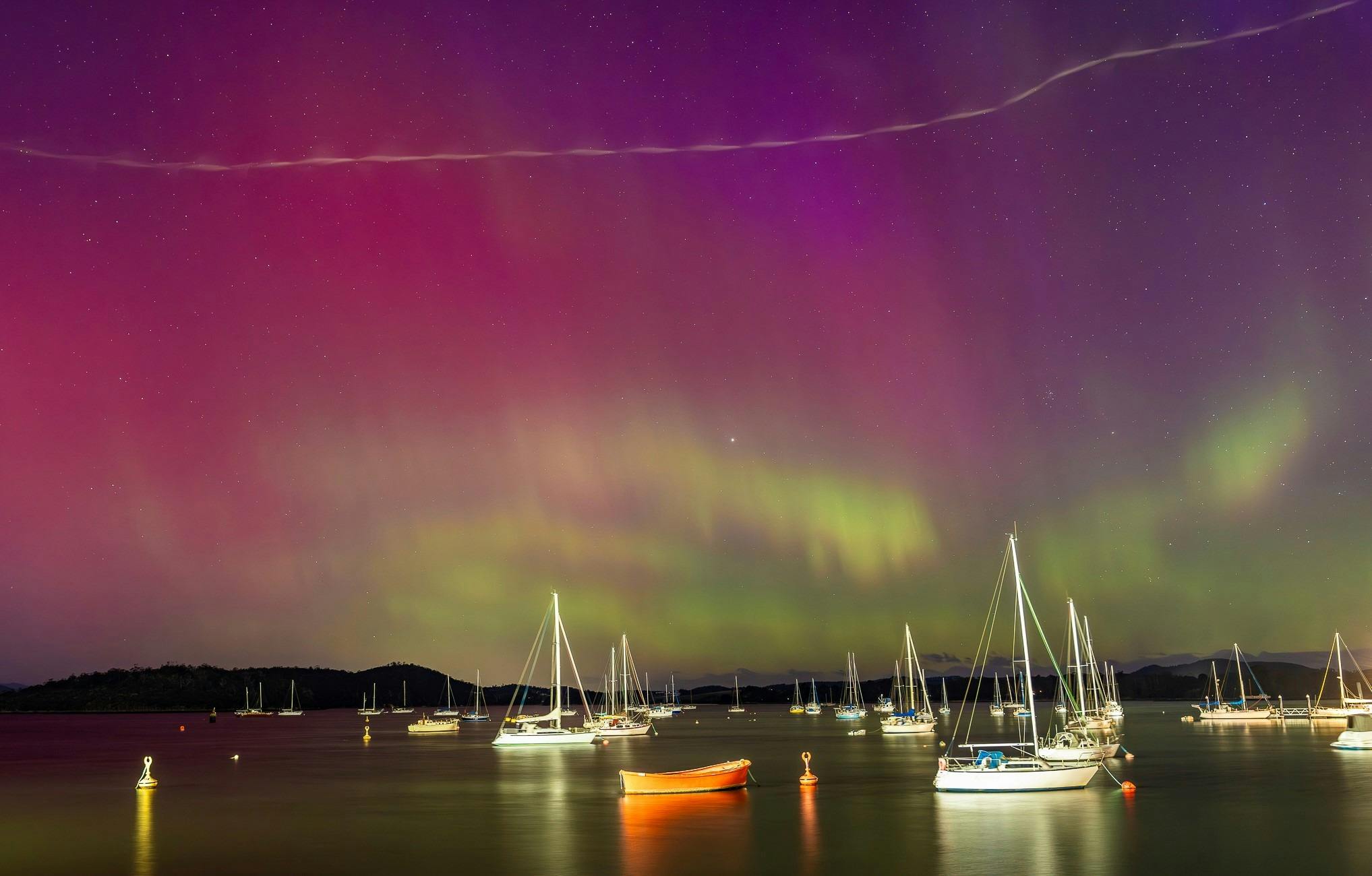 Sailboats on a calm bay against a backdrop of shimmering Northern lights