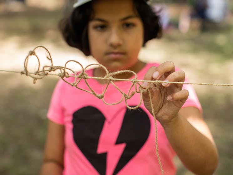 A teenager in a pink tshirt string weaving using traditional Aboriginal methods in a workshop