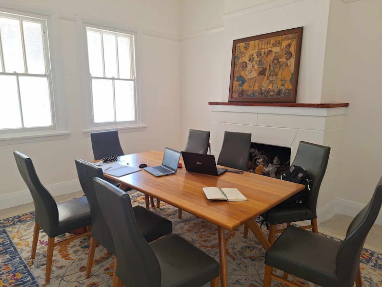 Meeting Room with board table and eight chairs. Laptops and paperwork on table. Painting on mantle.