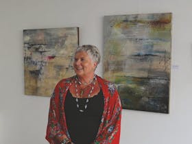 Juan posing in front of paintings. She is wearing a red wrap covering her black top with 3 necklaces