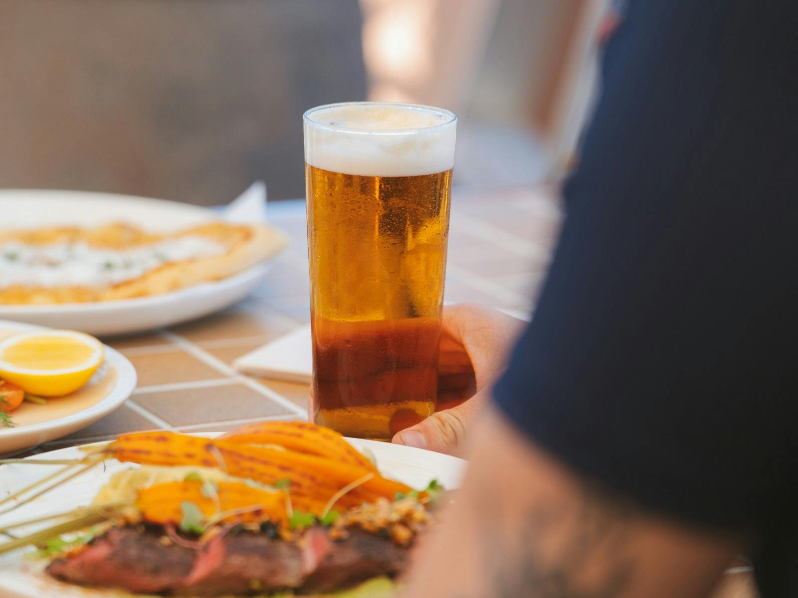 Glass of cold beer on a table with pub meals including steak and seafood in a relaxed dining setting Glass of cold beer on a table with pub meals including steak and seafood in a relaxed dining setting
