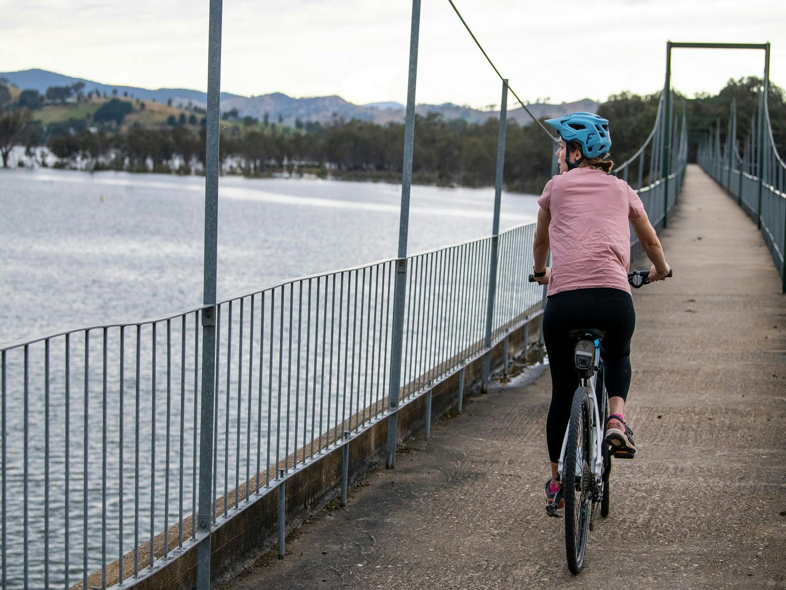 A solo cyclist rides across Bonnie Doon Bridge above Lake Eildon, framed by scenic views.