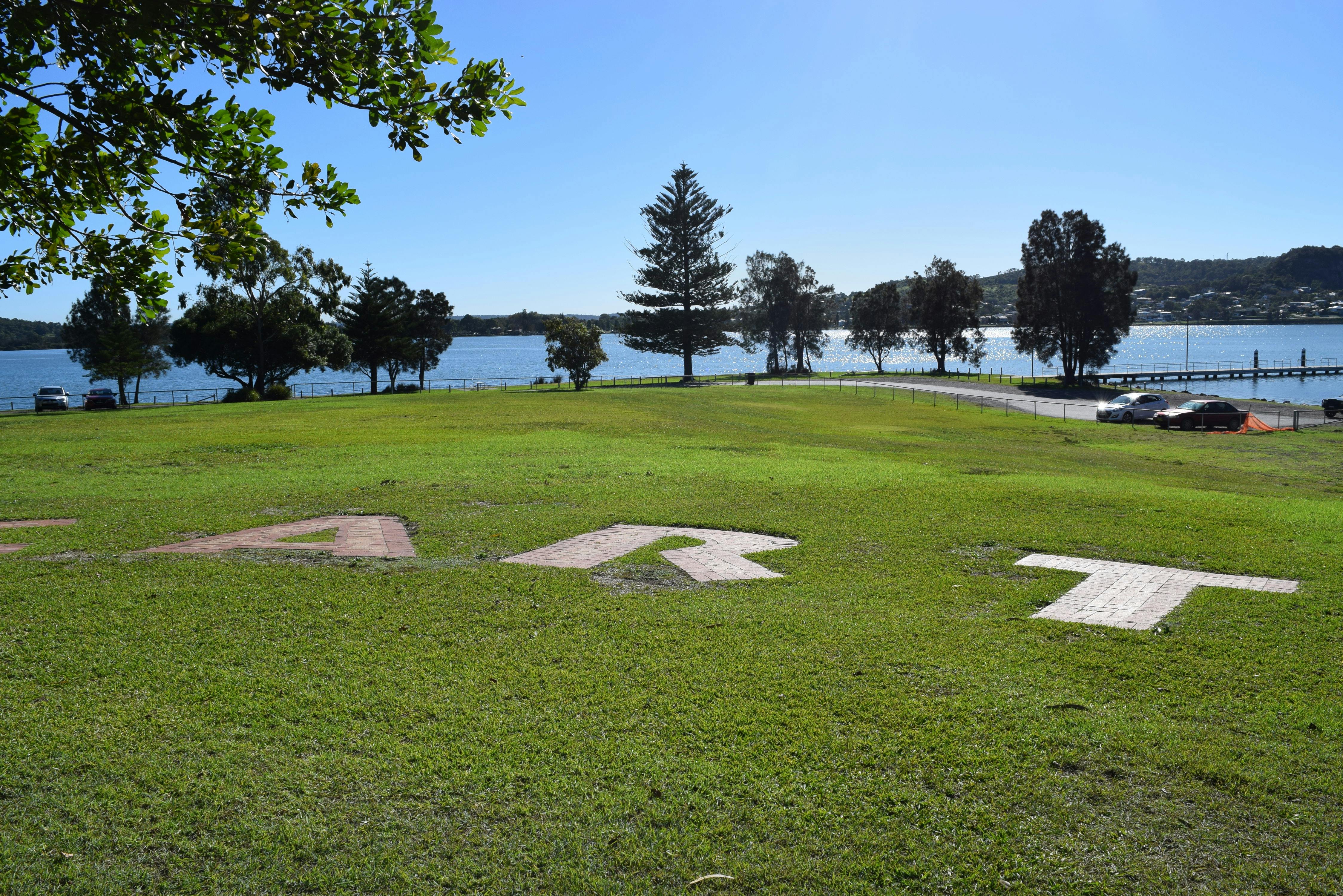 A detail of Richard Tippings Hear the Art sculpture words ART seen in grass with Lake in background