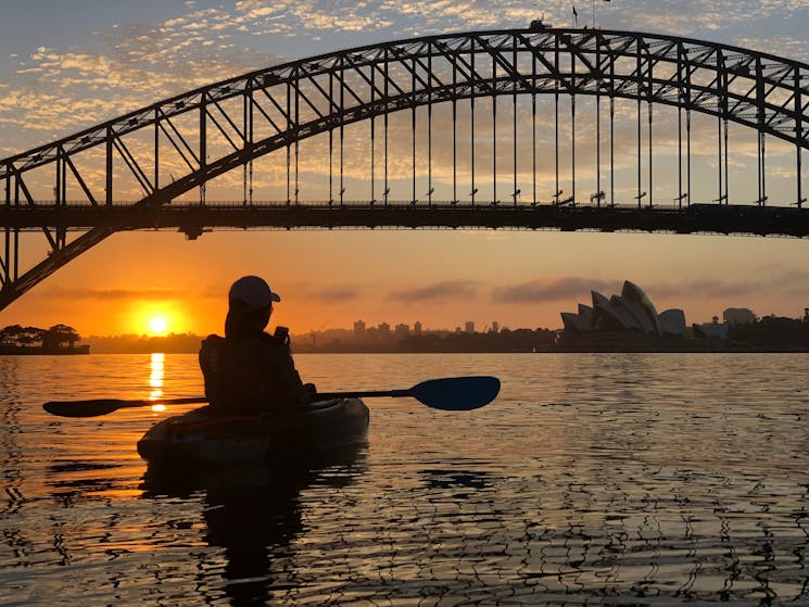 Silhouette of solo paddlers sitting on a calm Sydney Harbour with bridge and Sydney Opera House