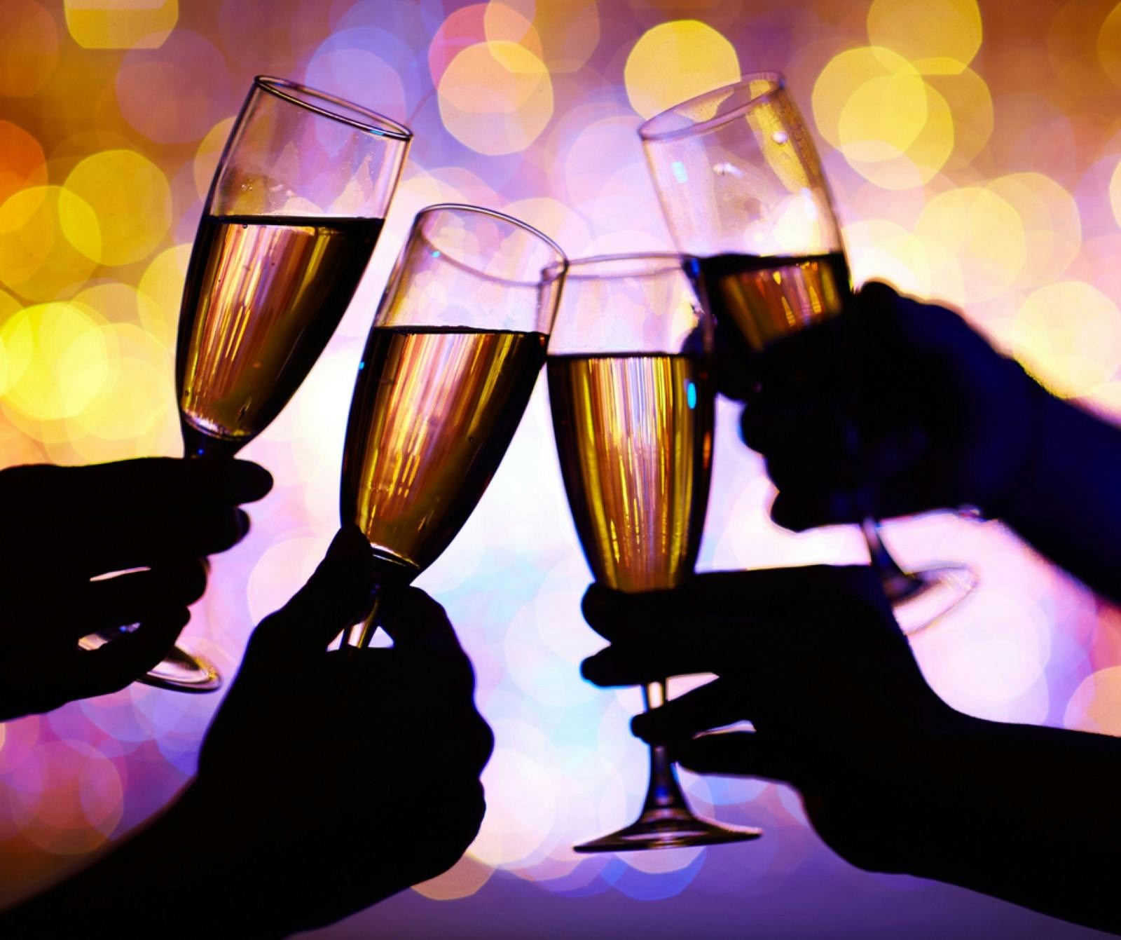 four wine glasses clinking with bright lights in background