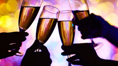 four wine glasses clinking with bright lights in background