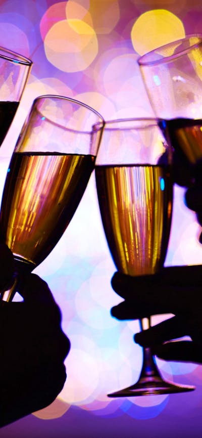 four wine glasses clinking with bright lights in background
