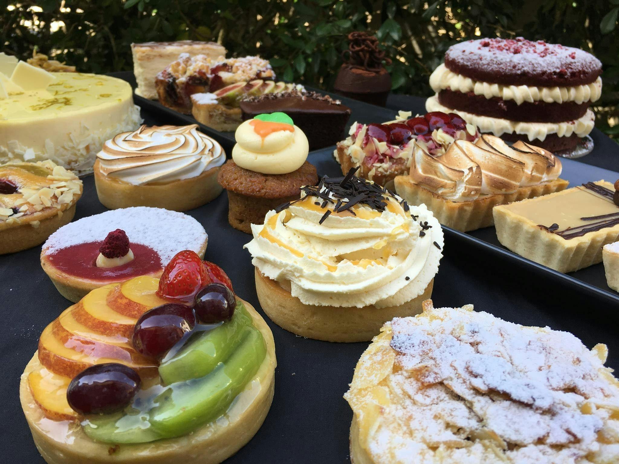 A selection of pastries and cakes sitting on a table in front of a hedge A selection of pastries and cakes sitting on a table in front of a hedge