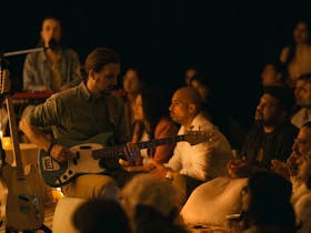 Man seated in a crowd playing guitar