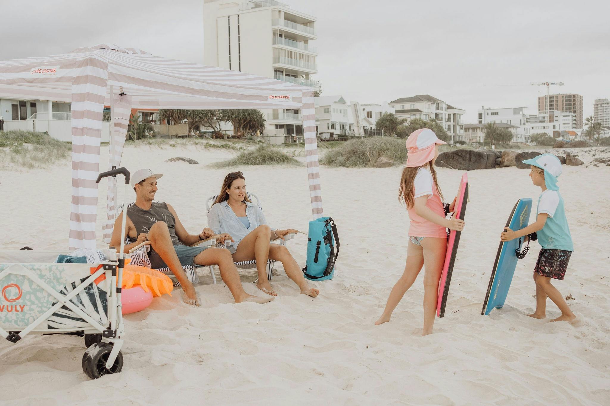 Family on beach under Cabana, relaxing on chairs, children on bodyboards