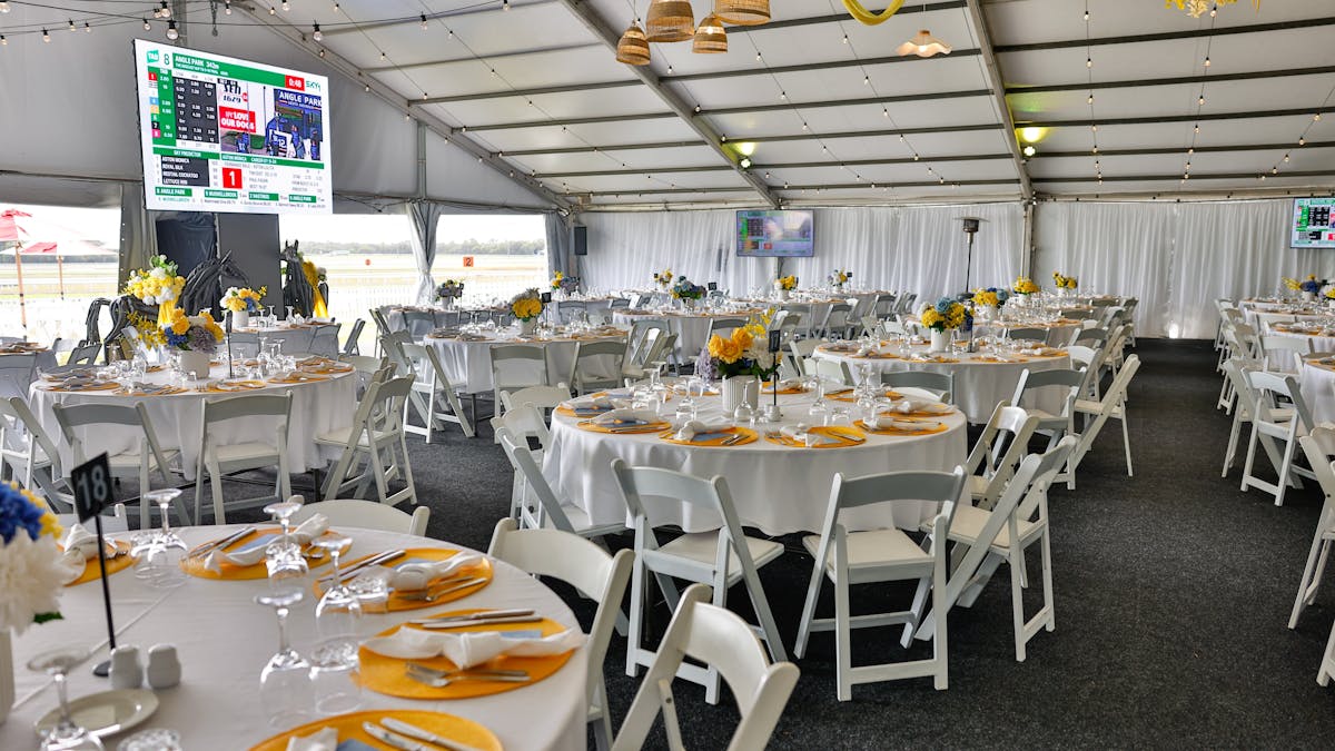 Large undercover marquee with large round tables set for dining styles with florals