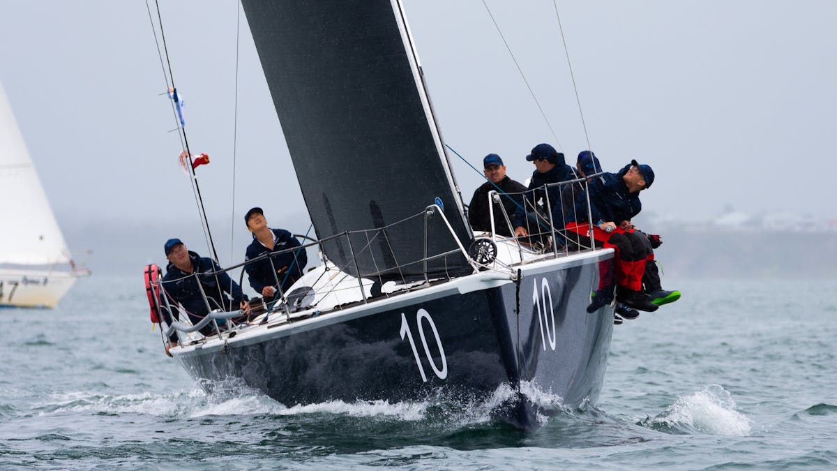 Sailors sitting along the edge of a yacht with black sails as it races through the water.
