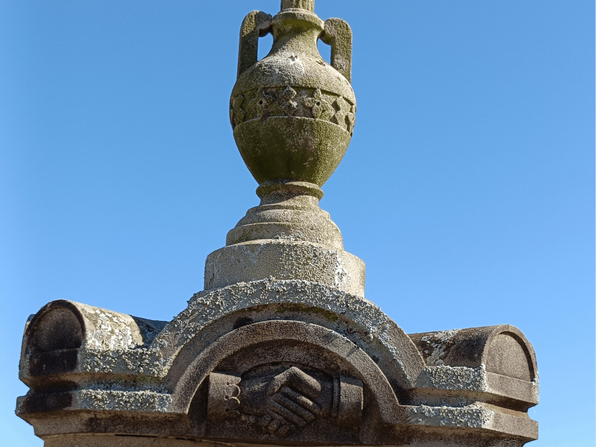 Two clasped hands, etched in sandstone. The left cuff is frilled and feminine, the right is manly.