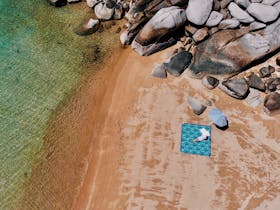 Picnic rug on a beach with rocks in the corner.