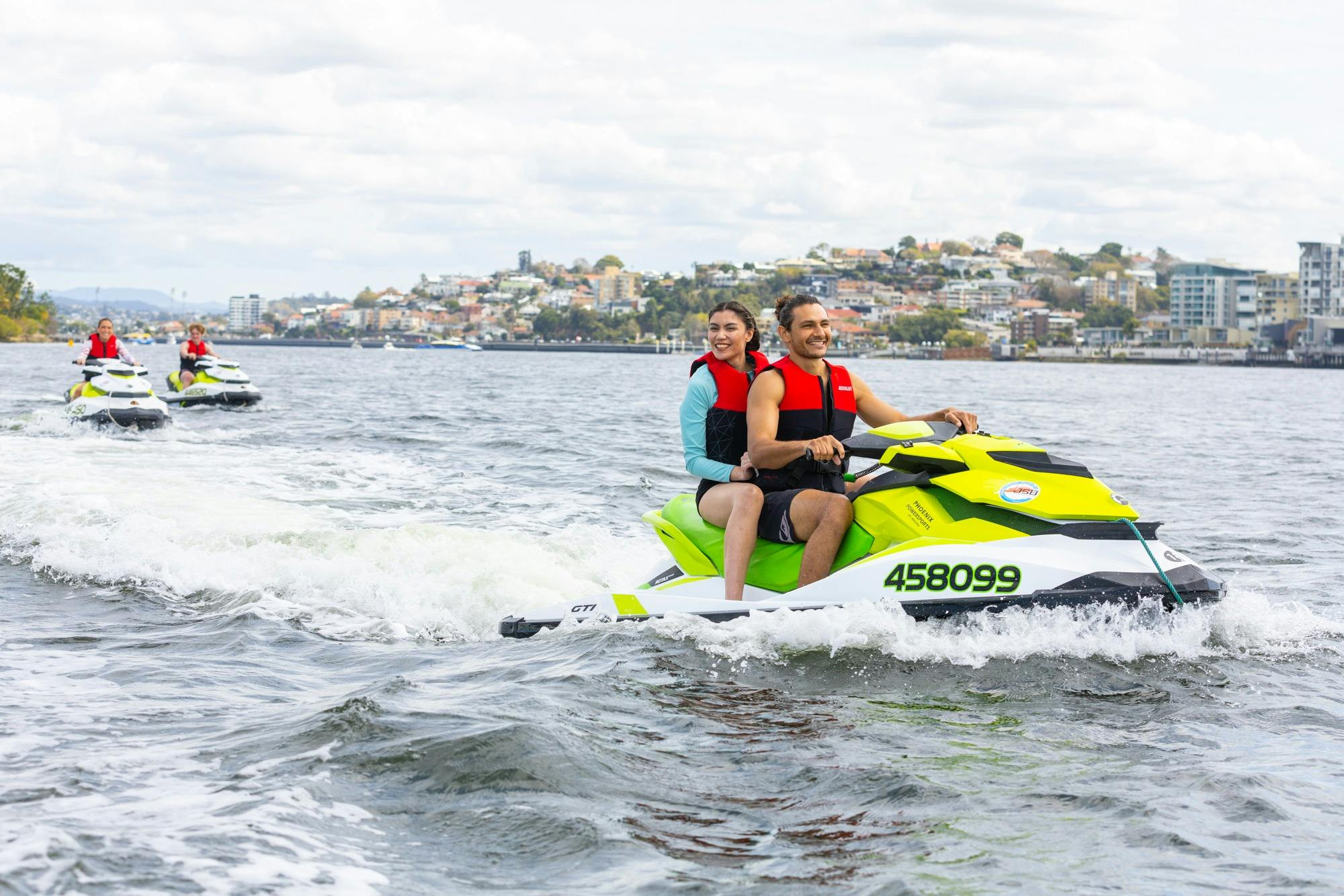 A group of people riding jet skis along the Brisbane River smiling.
