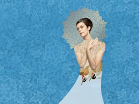 A beautiful woman wearing a white dress, with birds on it, standing against a blue floral background