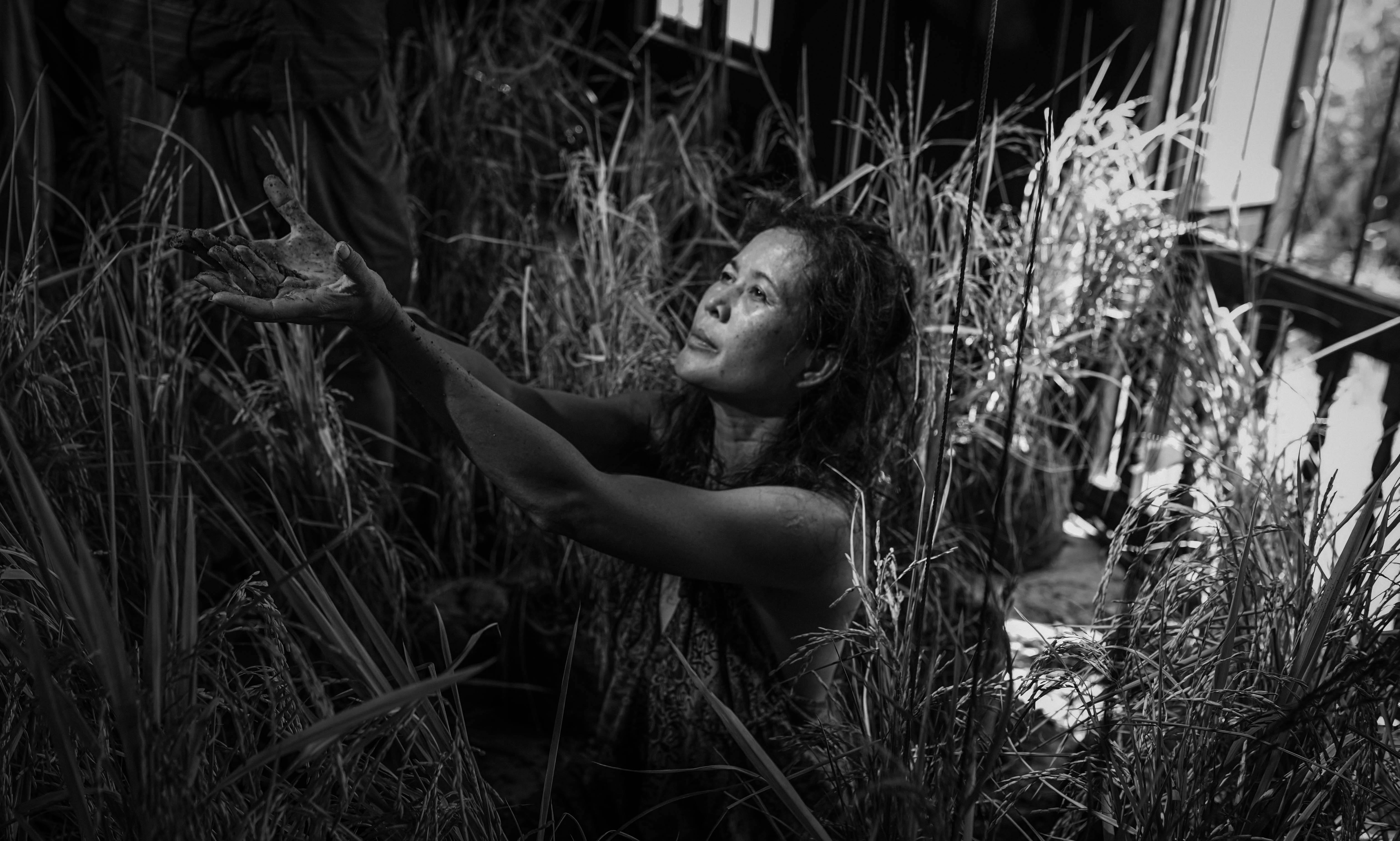 Black and white image of woman reaching hands up to left of image with grass in background