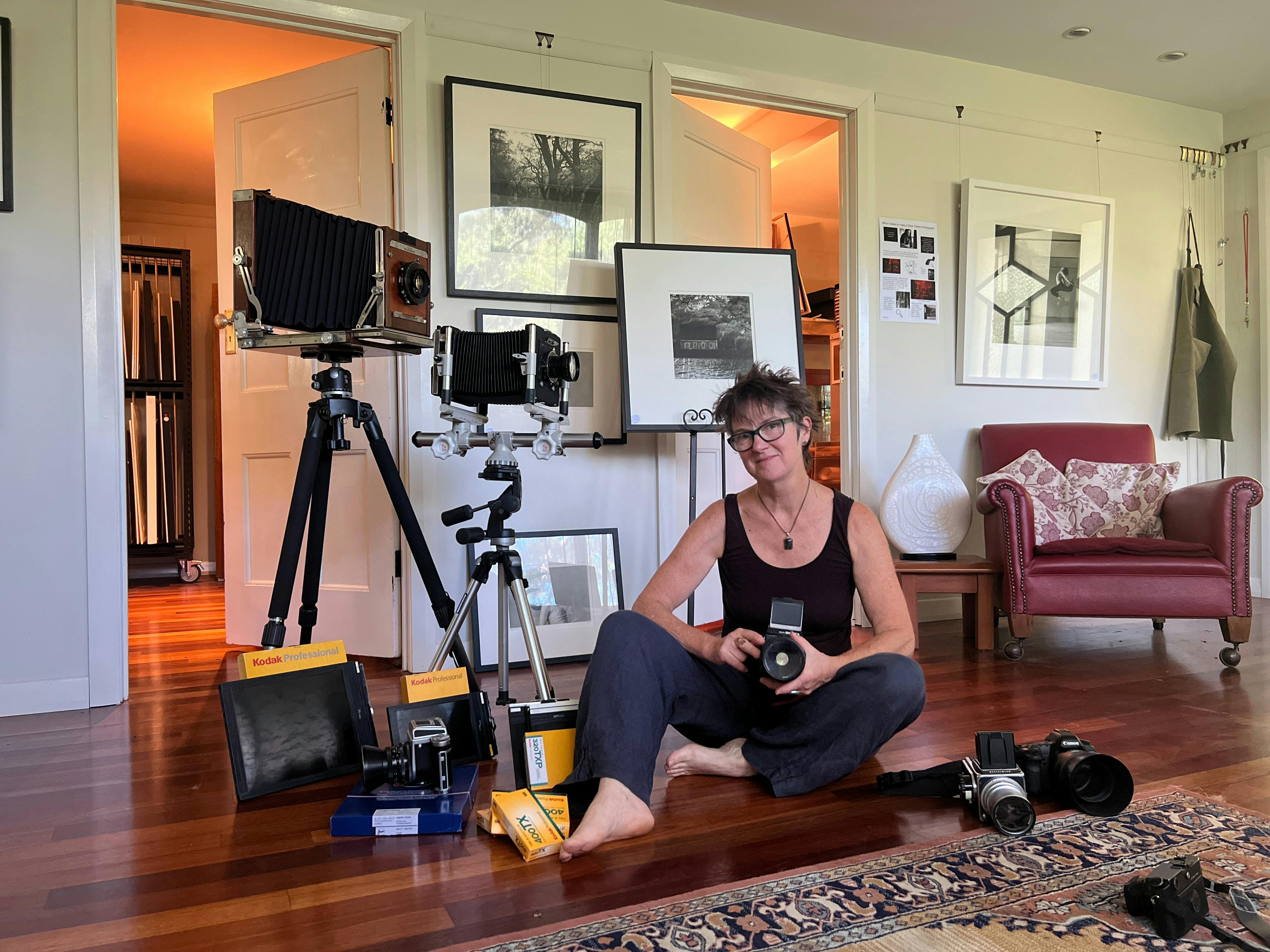 Photographer sits among vintage film cameras, tripods and framed black & white prints in her studio
