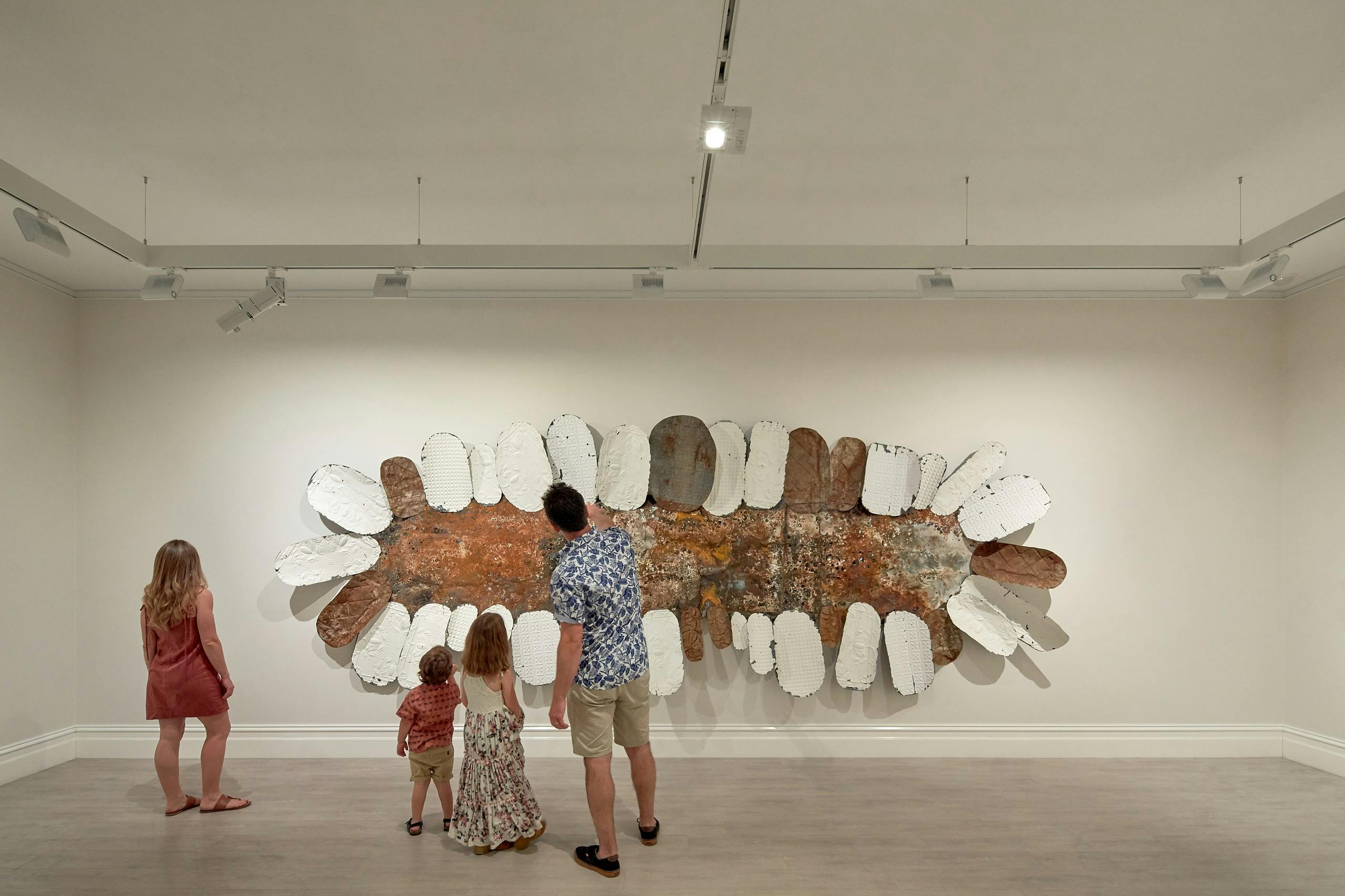 Tin sculpture on the wall of an art gallery with a family of 4 walking past