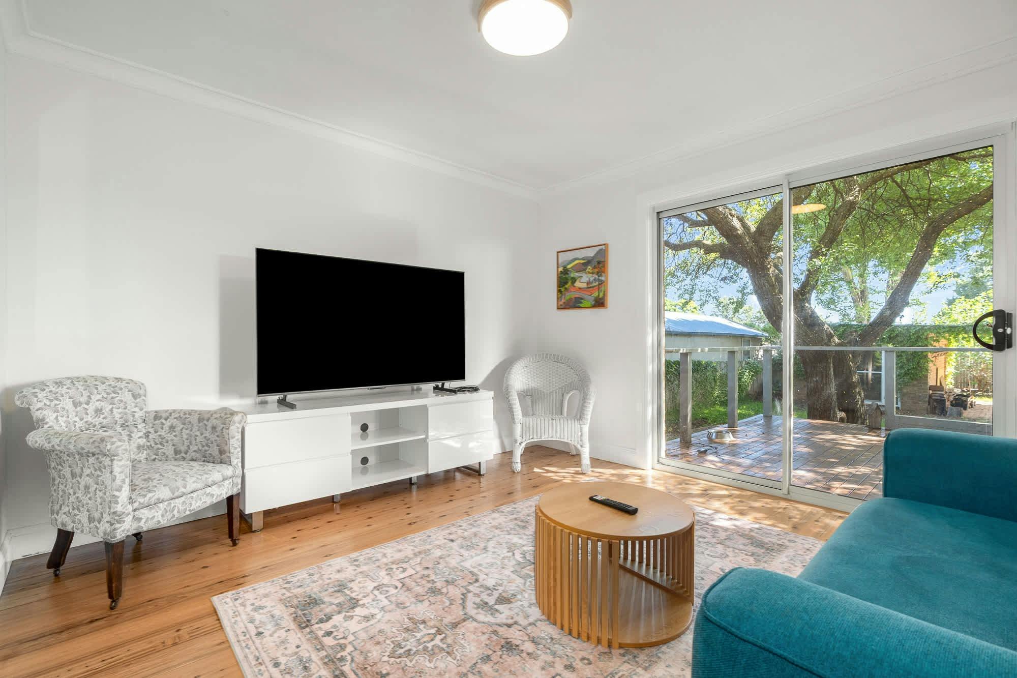 Living room with tv, entertainment unit, blue couch, coffee table, rug and doors out to deck