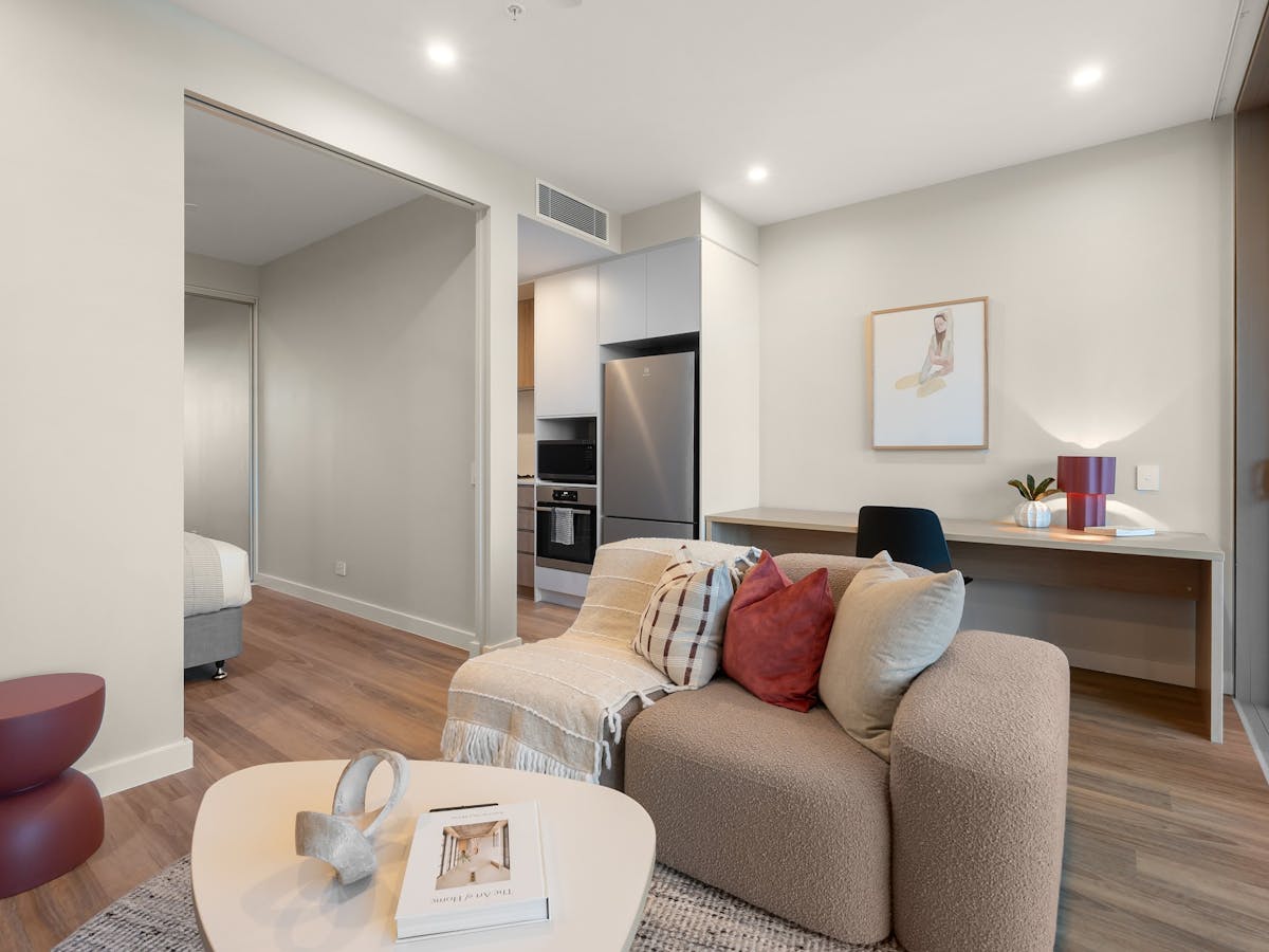 Living area with brown couch and red cushions, oval shaped coffee table and desk in the background.