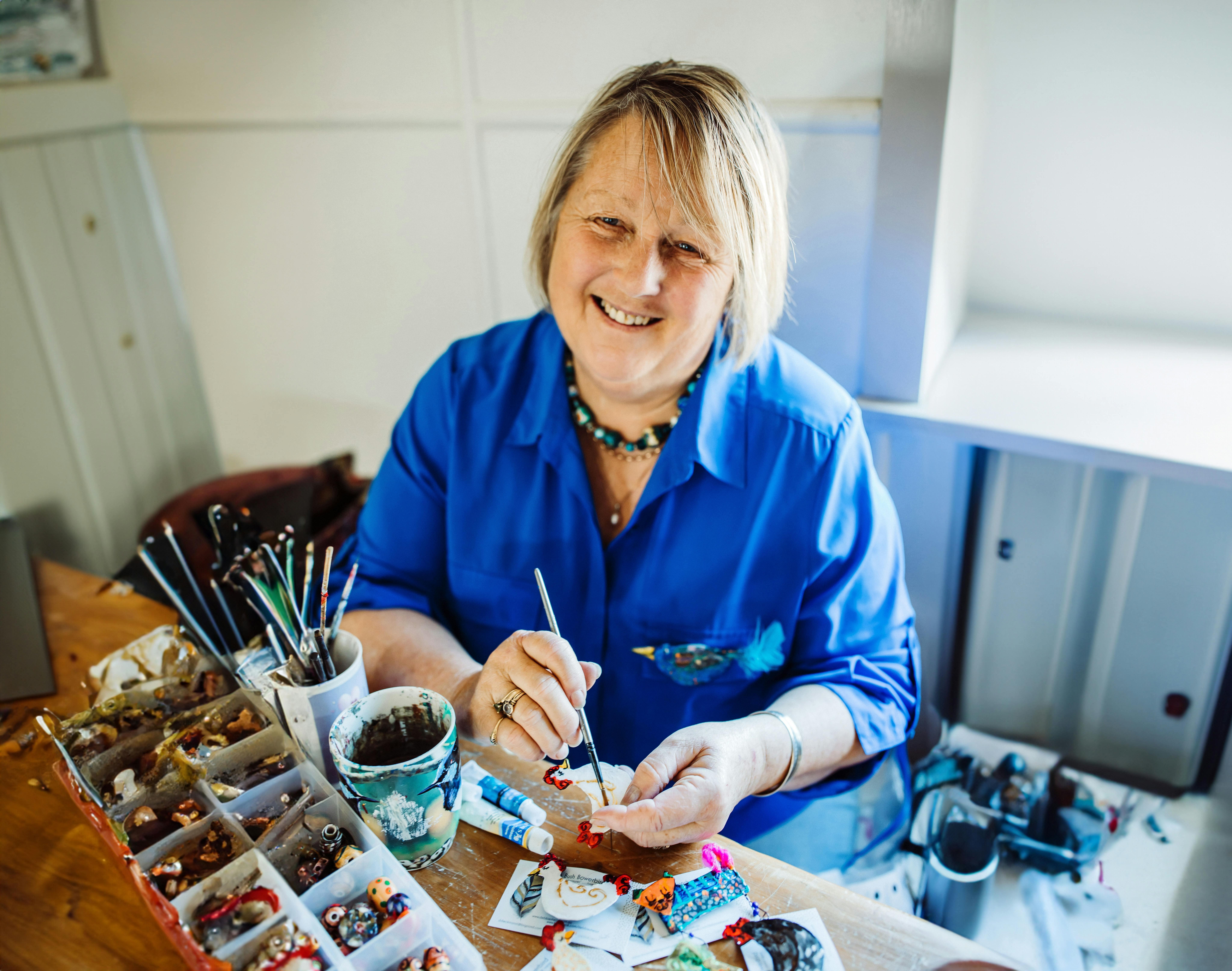 Artist Debbie Dieckmann pictured in her art studio creating brooches in blue shirt