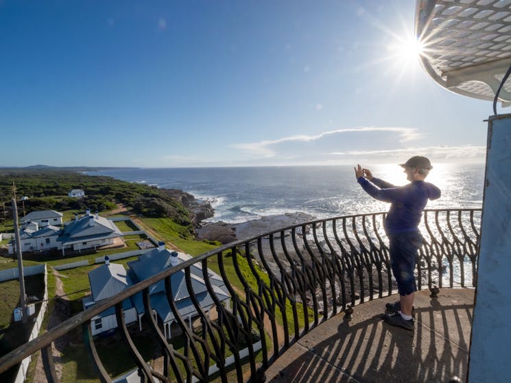 A guest is taking a phone photo from the top of the light house over looking ocean and cottages