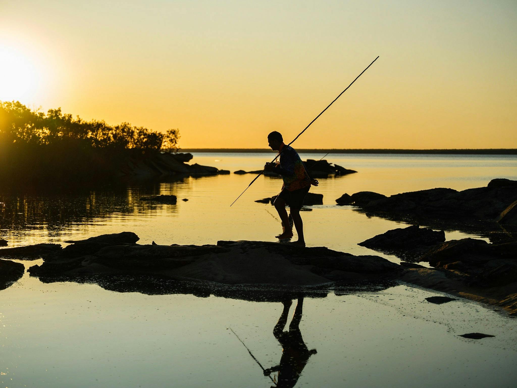 A figure walking across the mangroves hunting for fish with spear.