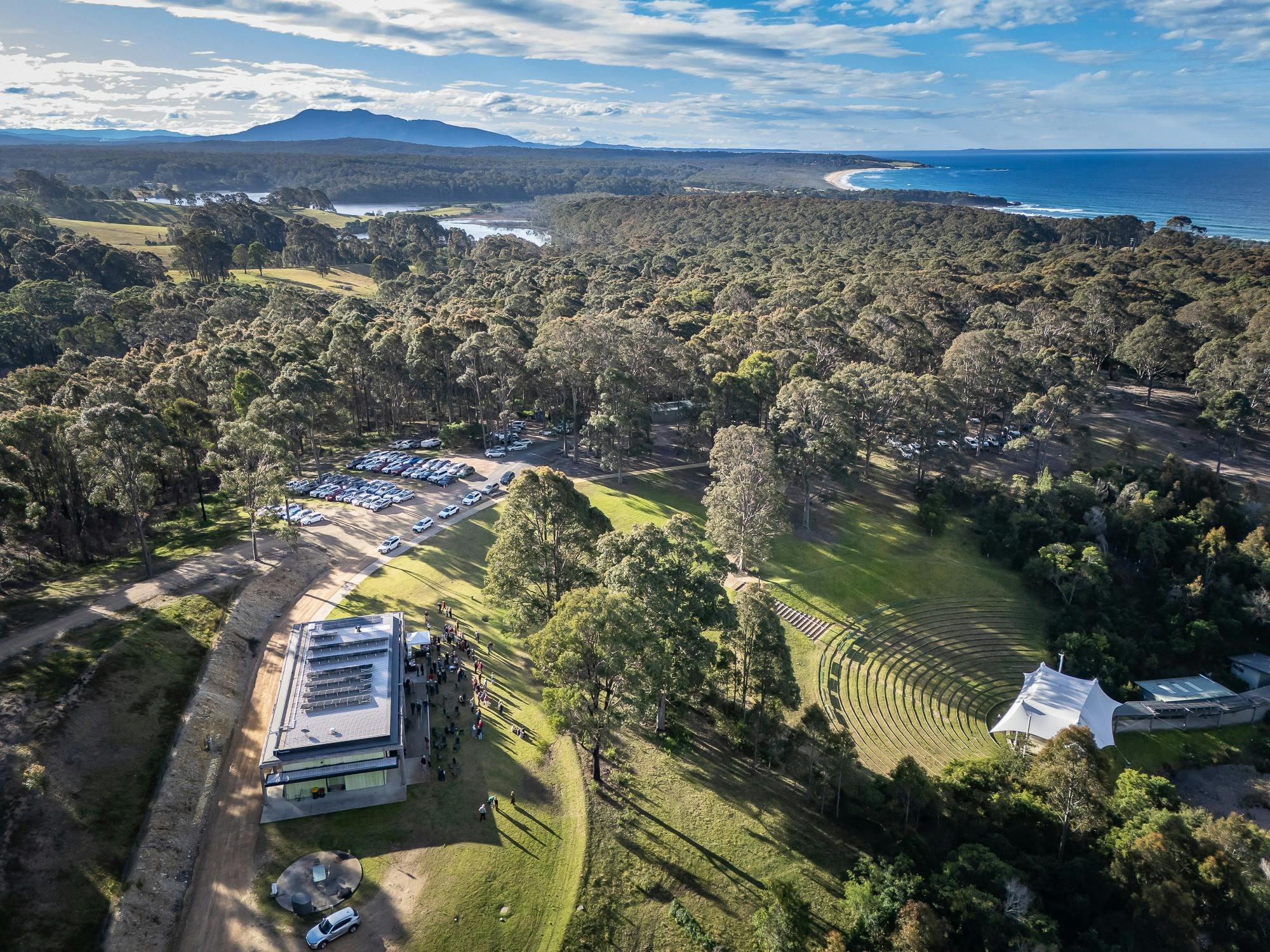 Drone image of the Four Winds Venue featuring bushland, water and mountains