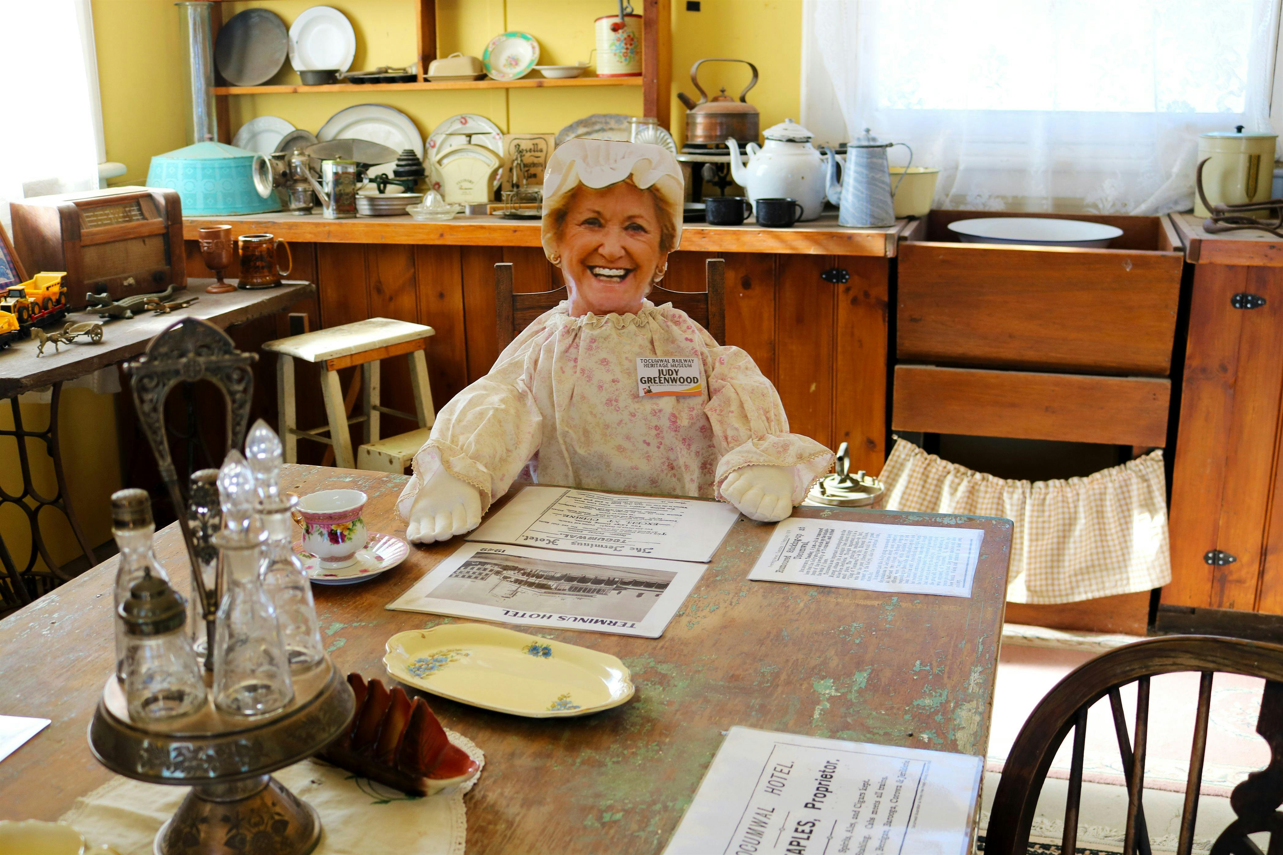 Museum interior, featuring a set table and dressed mannequin seated at table.
