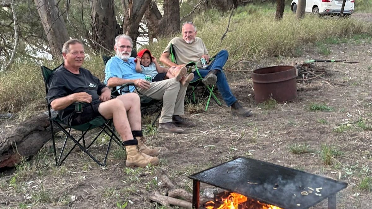 4 people sitting around a camp fire on the banks of the river at Ticklemans Gardens