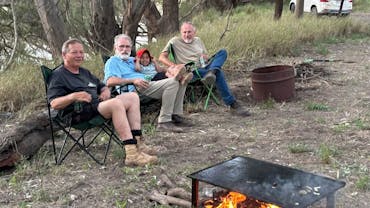 4 people sitting around a camp fire on the banks of the river at Ticklemans Gardens