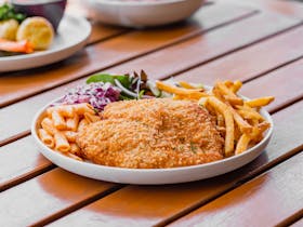 Plate of chicken schnitzel with fries, salad, and pasta on a wooden table at the Pastoral.