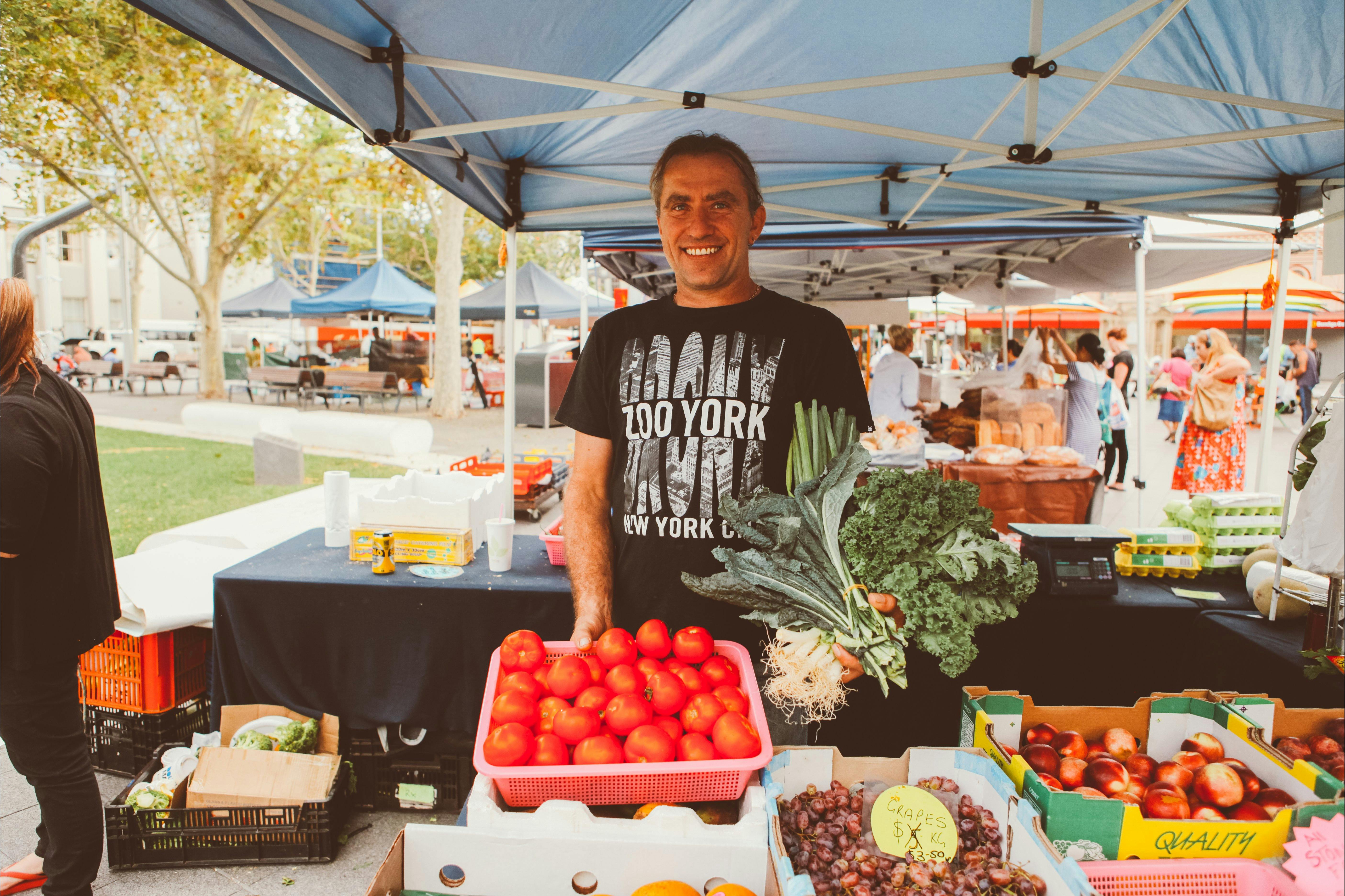 Troy from Kemps Creek Farm with his stall of organic fresh fruit and vegetables. Troy is holding a bunch of leafy greens.