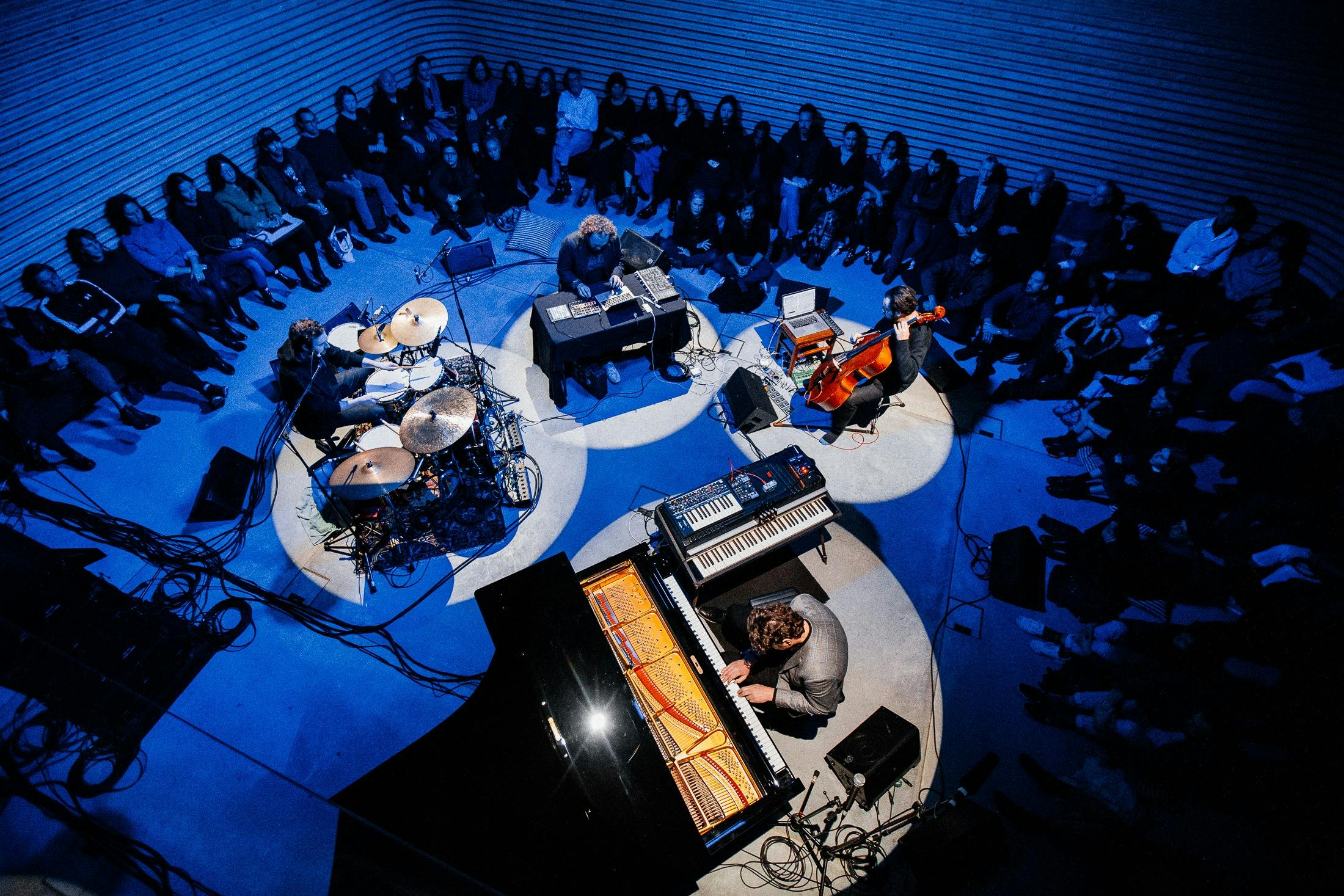 Birds eye view of a four piece jazz band perform with a crowd seated around them