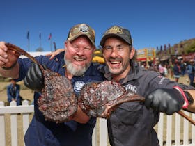 Two men hold bbq meat and smile at the camera