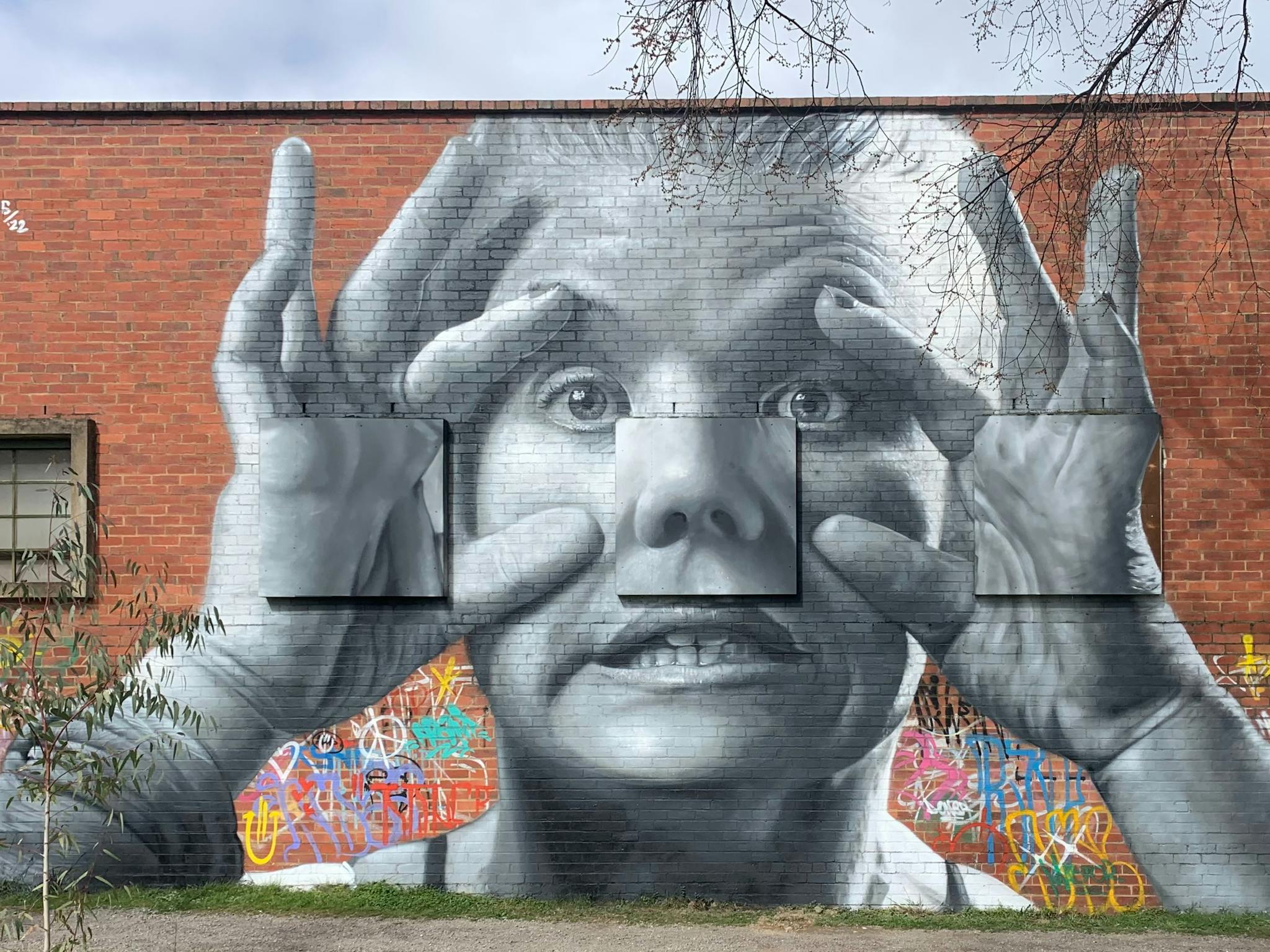 Mural of a face peering out curiously, with hands holding eyes wide. Painted by Damien Mitchell